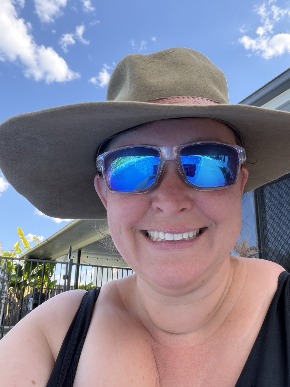 Rachel smiling outdoors in a wide-brimmed hat and blue sunglasses