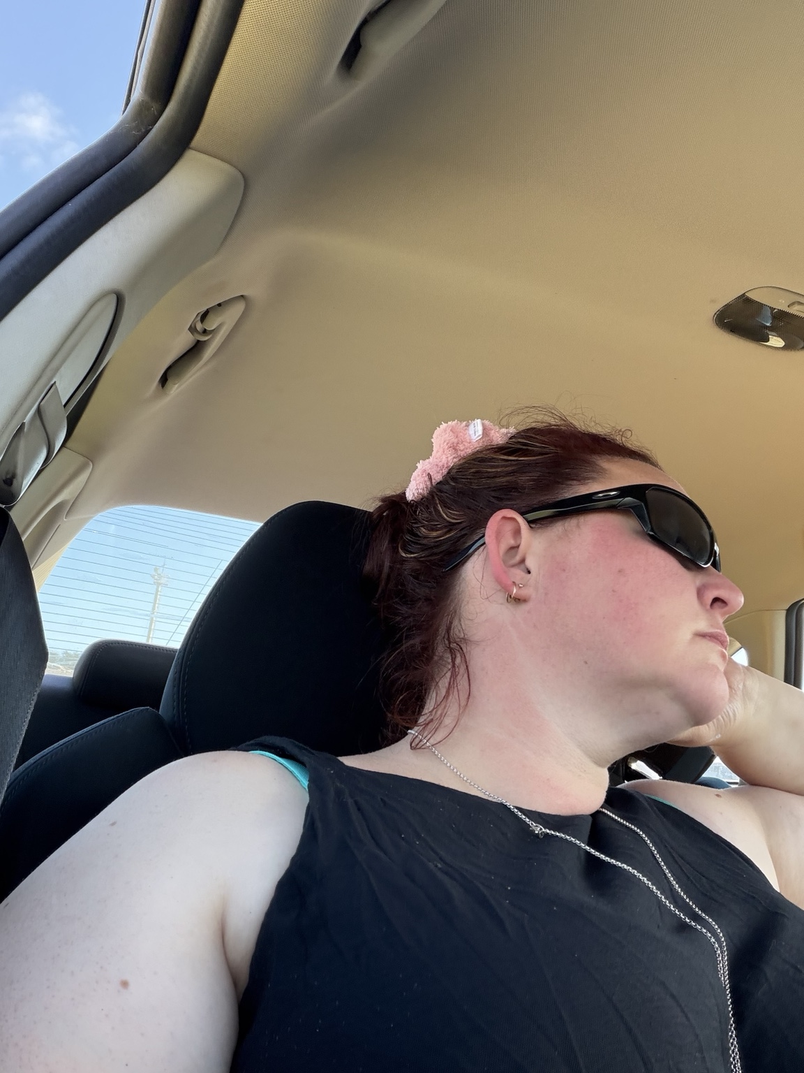 Rachel resting in the passenger seat of a car, wearing dark sunglasses
