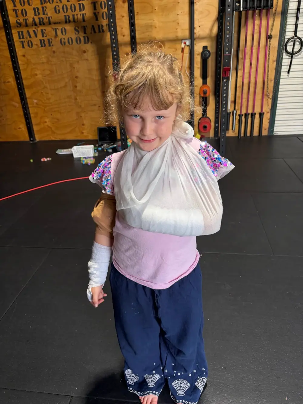 A young child in a First Aid 2 U practice scenario wearing an arm sling and a bandaged hand.